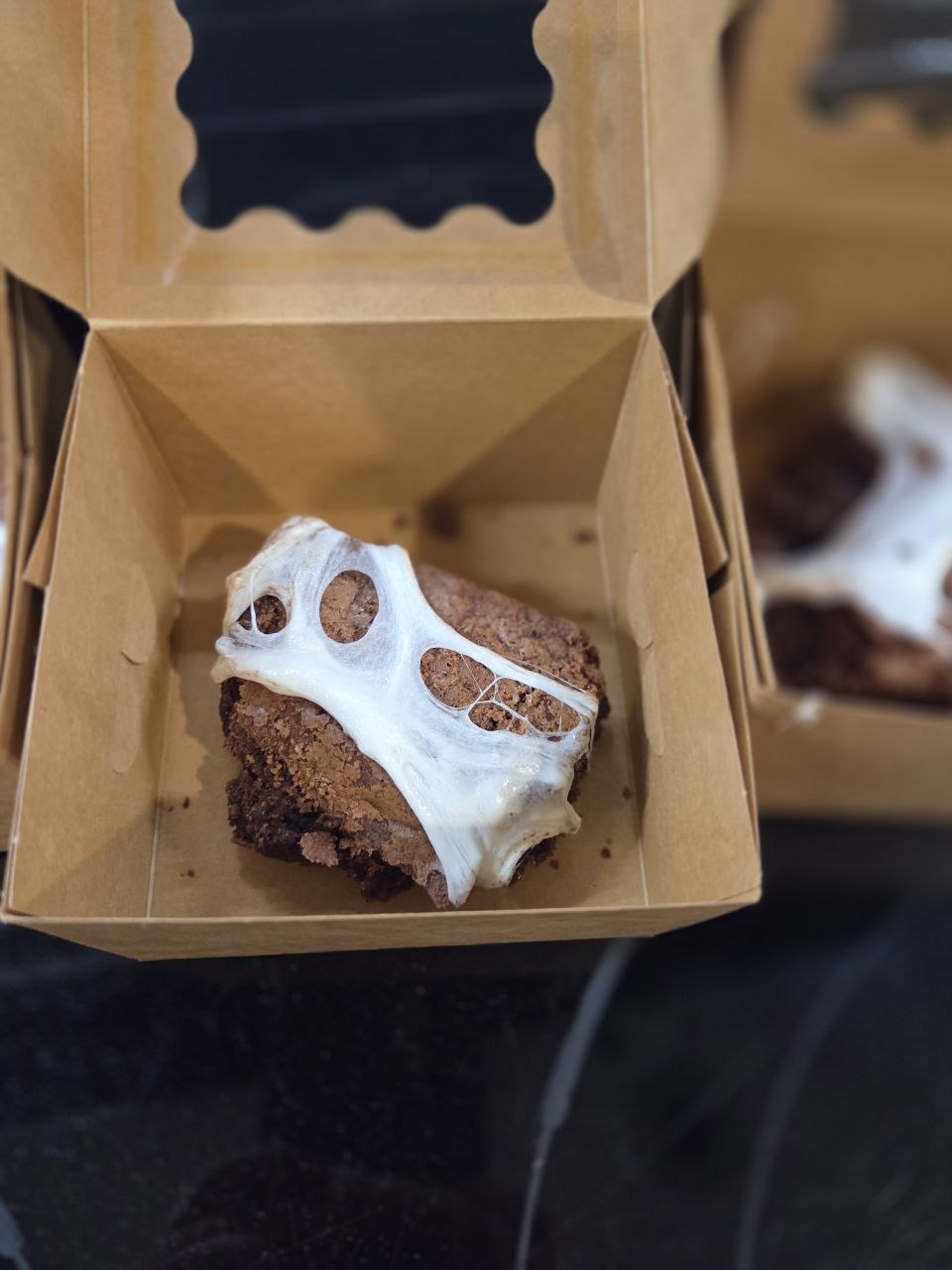 Fudgy brownie topped with a stretchy white marshmallow spider web in a kraft bakery box