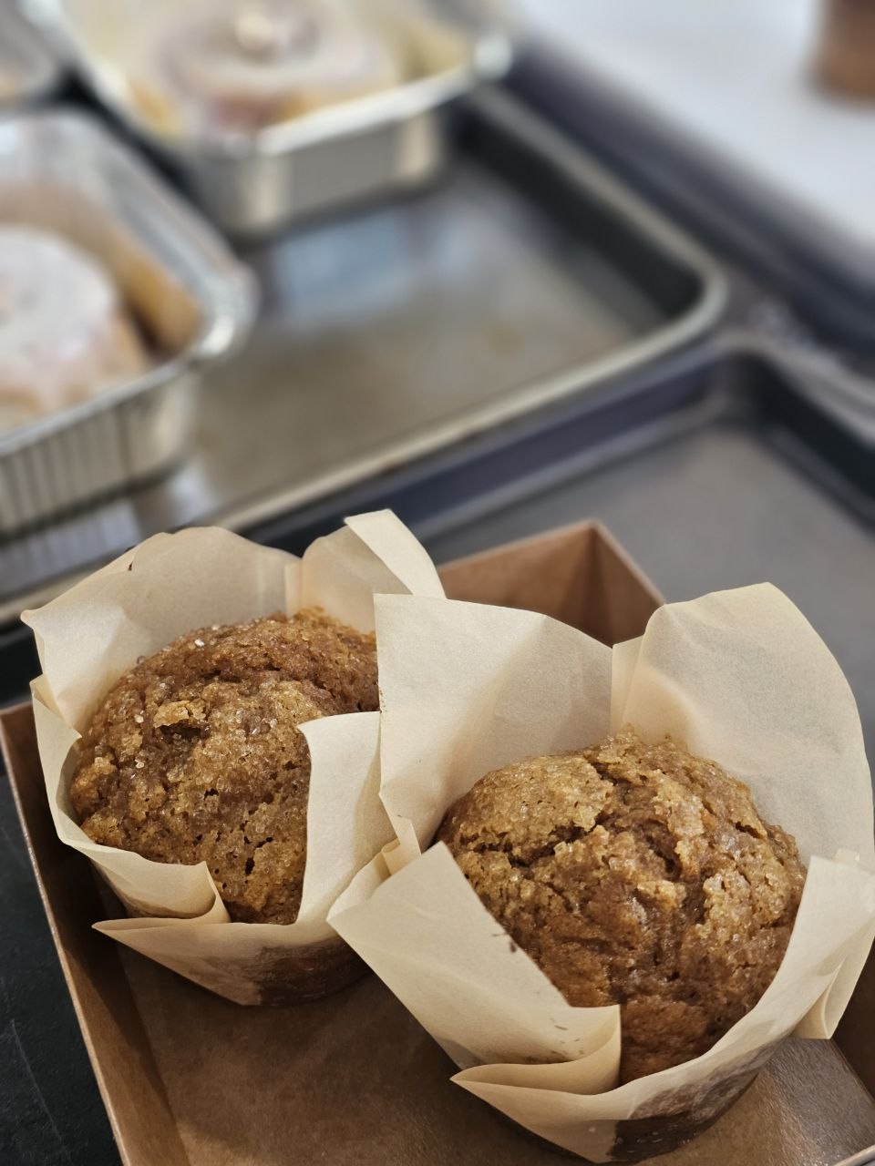 Two sugar-topped pumpkin muffins in parchment tulip liners in a kraft box