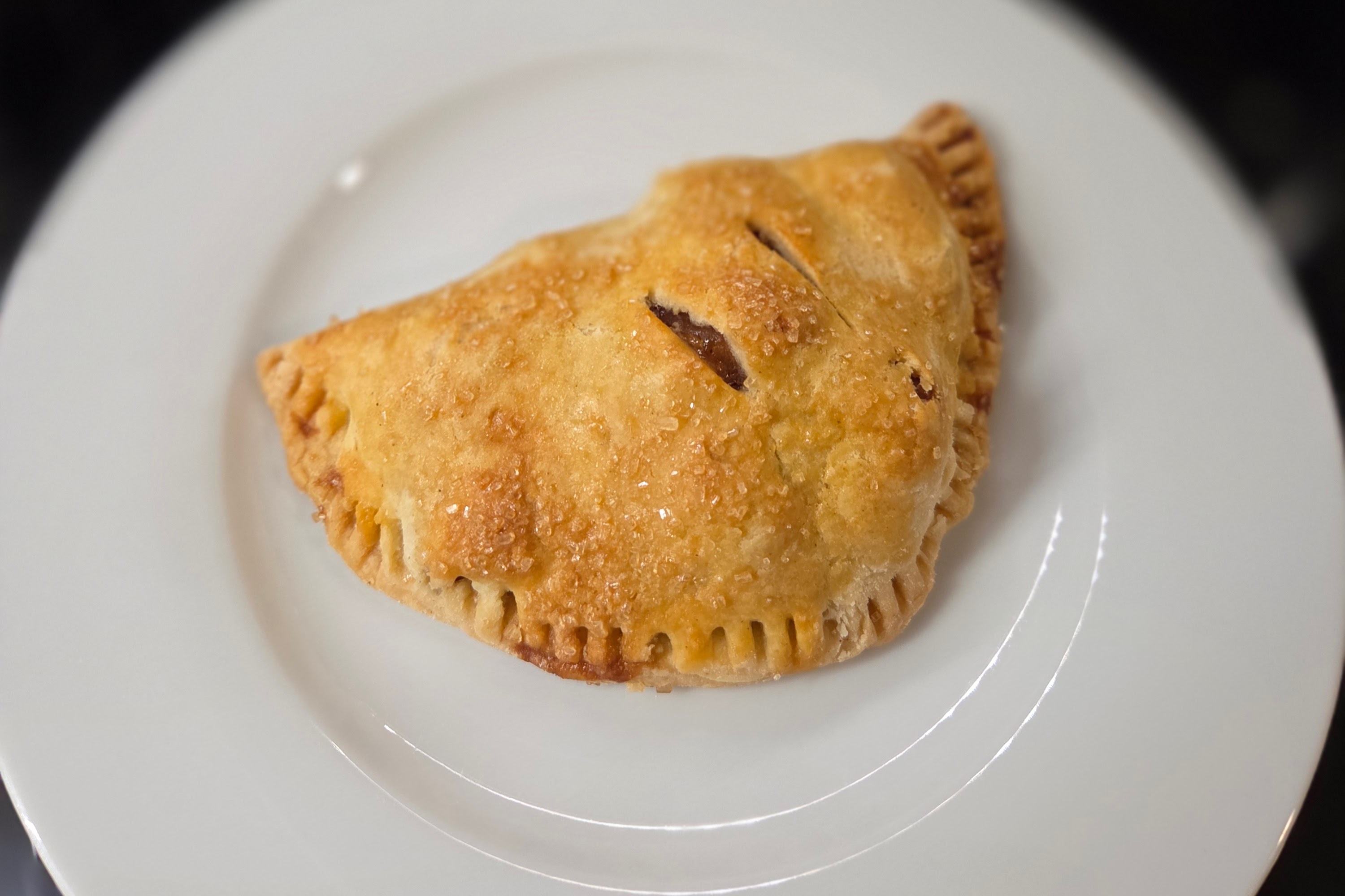 Apple hand pie with a crimped edge and sugar-sprinkled golden crust on a white plate